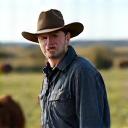 Portrait of Tom Fleming, a rancher, with cattle in the background.